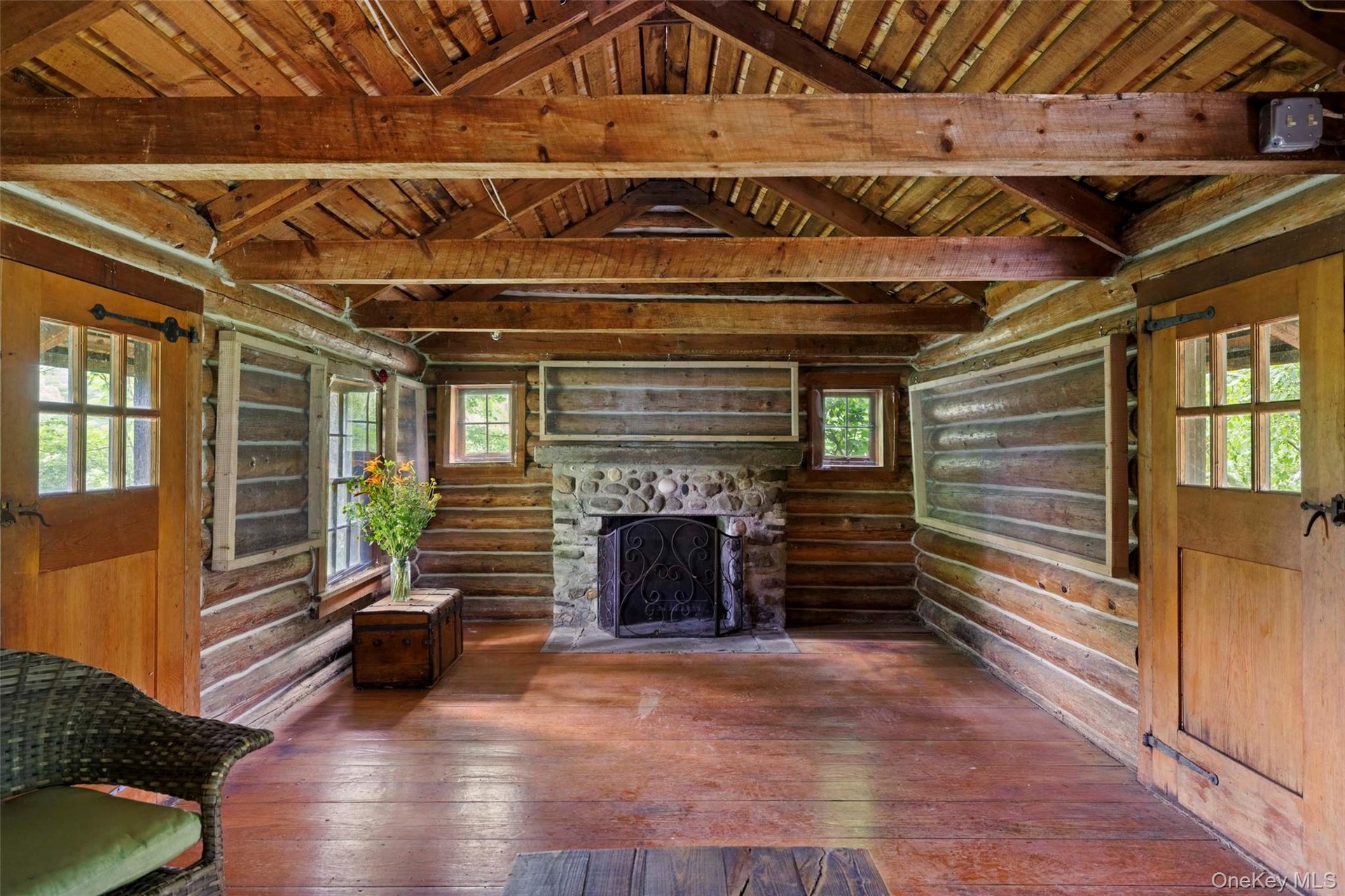 Rustic cabin interior with exposed log walls, hand-hewn beams, and a stone, wood-burning fireplace