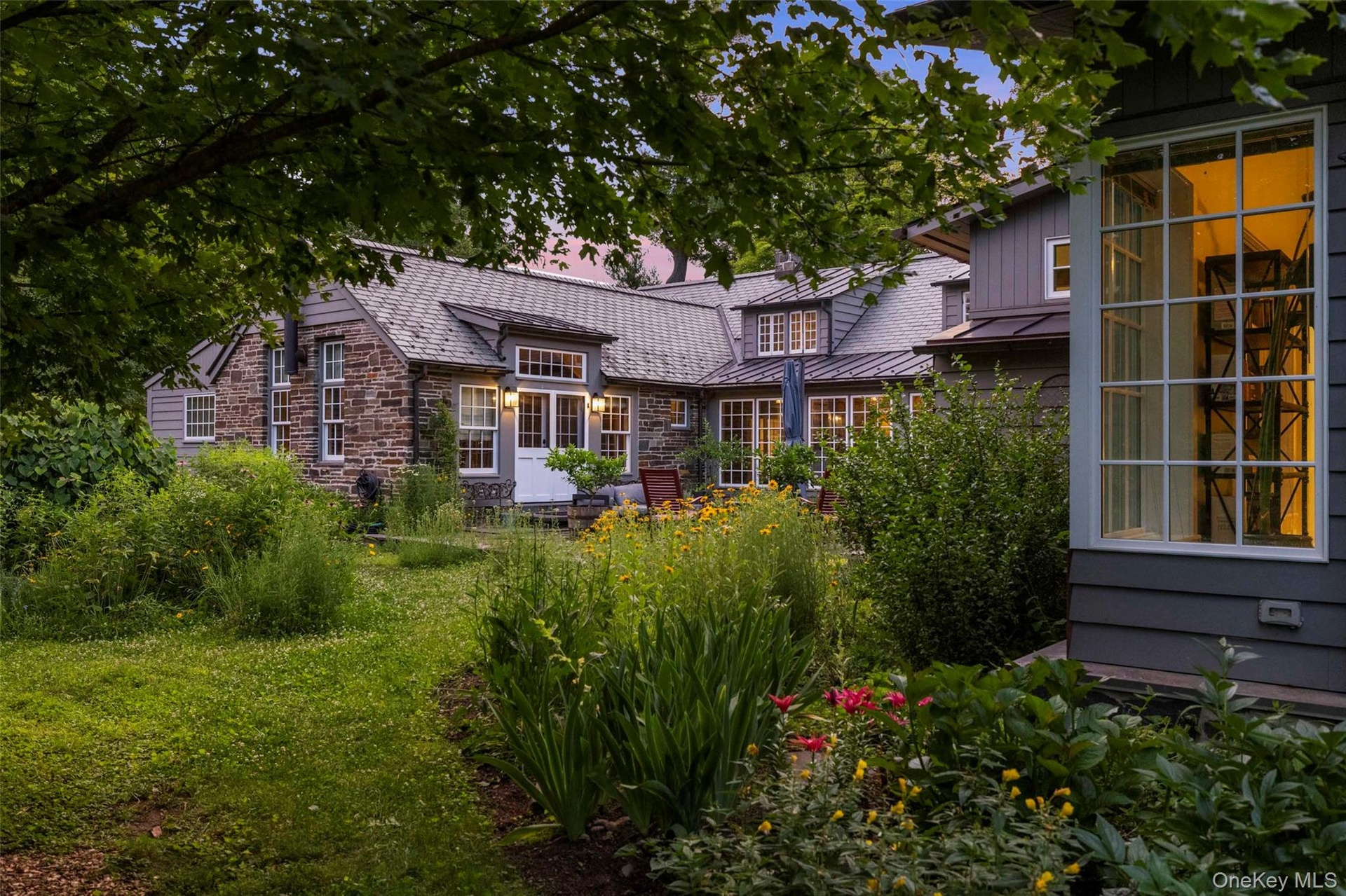 A beautifully landscaped courtyard transforms at dusk, creating an intimate outdoor setting surrounded by the warmth of the historic stone farmhouse a