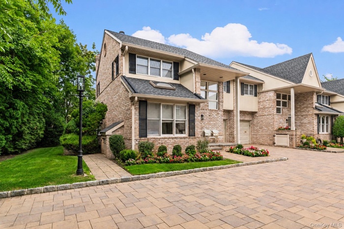 END UNIT Brick facade residence featuring a paver driveway, manicured landscaping, a paved walkway, and a decorative lamppost