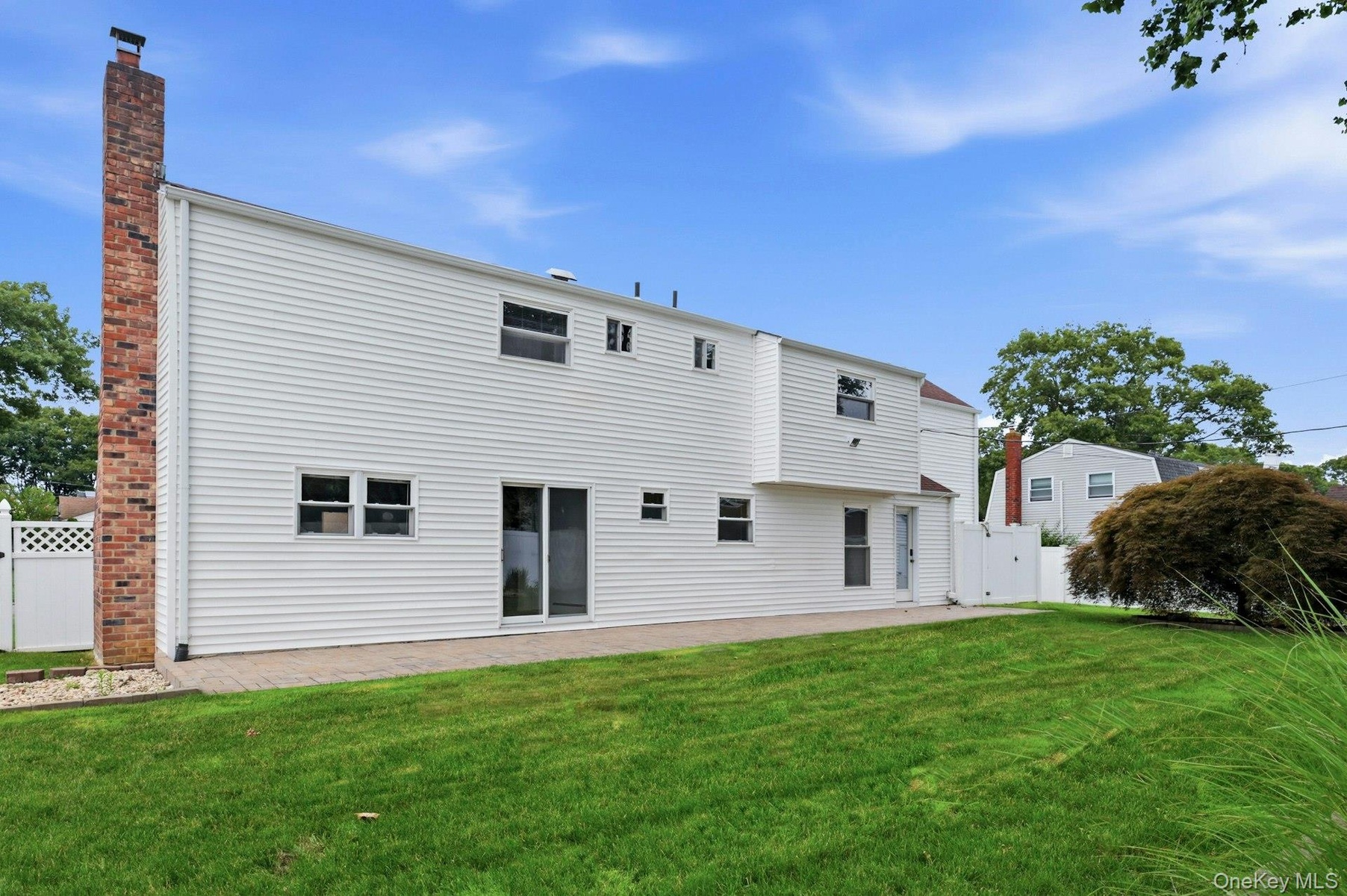 Rear exterior featuring white horizontal siding, a brick chimney, a ground-level patio, and a manicured lawn