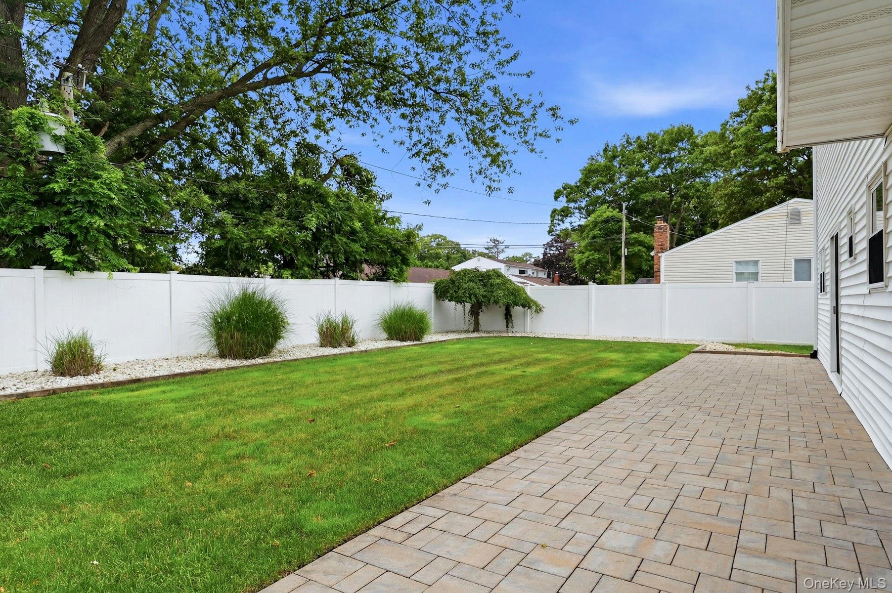 Expansive backyard featuring a paver patio, a lush lawn, and a white privacy fence