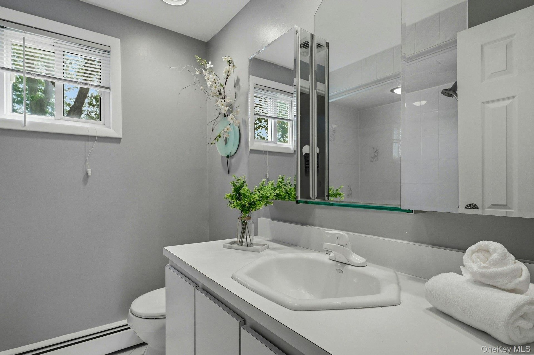 Bathroom featuring a white vanity with integrated sink, a medicine cabinet with mirrored doors, a window with blinds, and recessed lighting