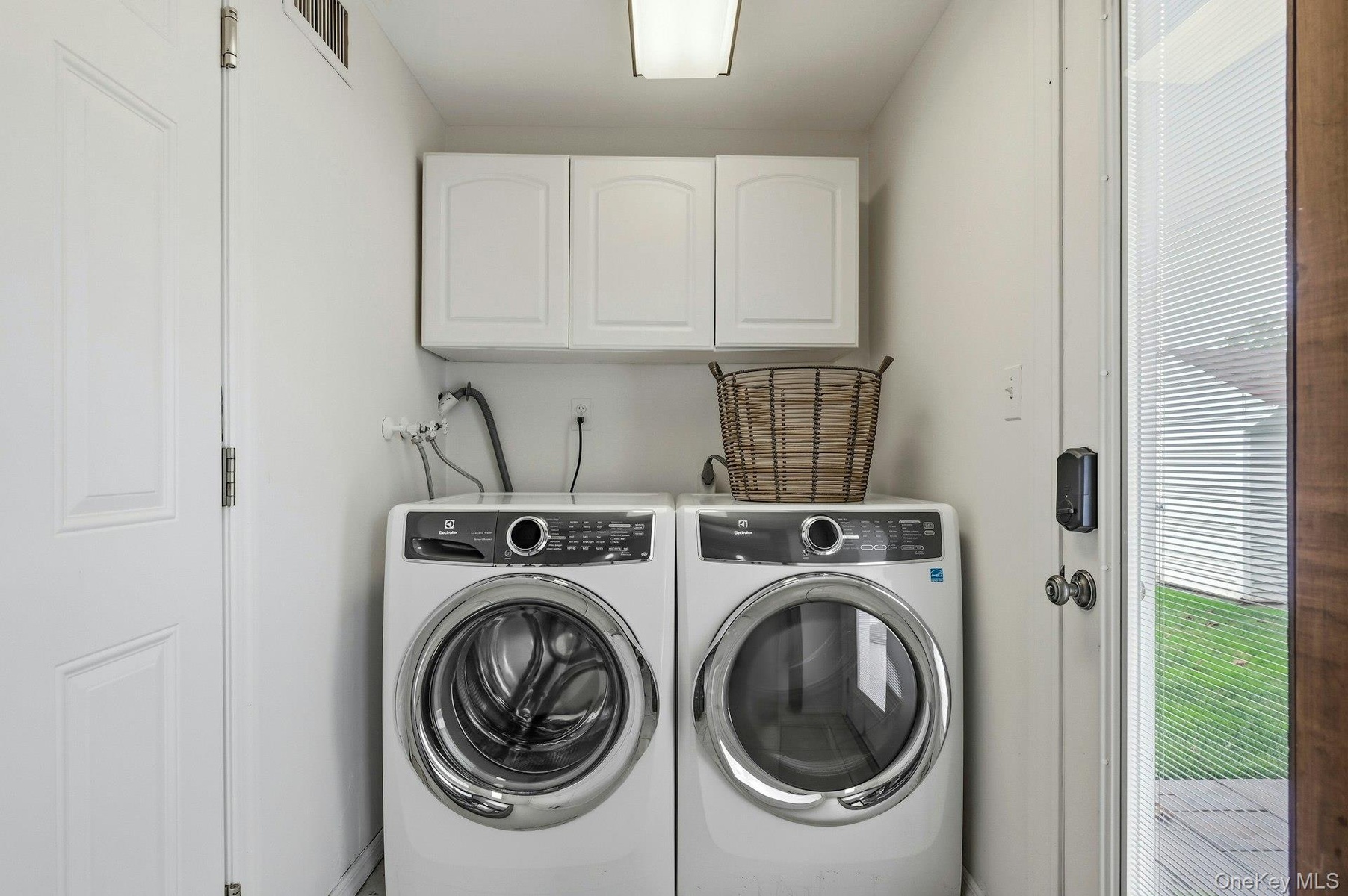 Dedicated laundry area featuring front-loading washer and dryer, upper cabinetry for storage, and a white paneled door