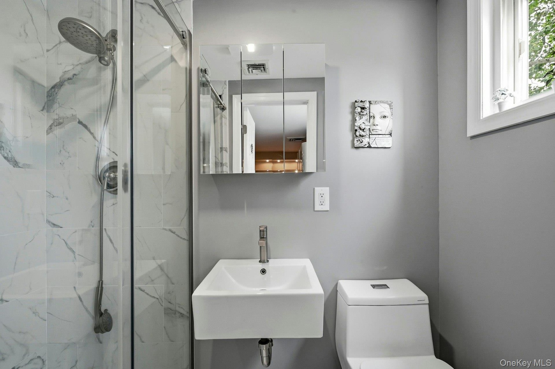 Sleek bathroom featuring a glass-enclosed shower with white marble-look tile, a wall-mounted rectangular sink, and a mirrored medicine cabinet