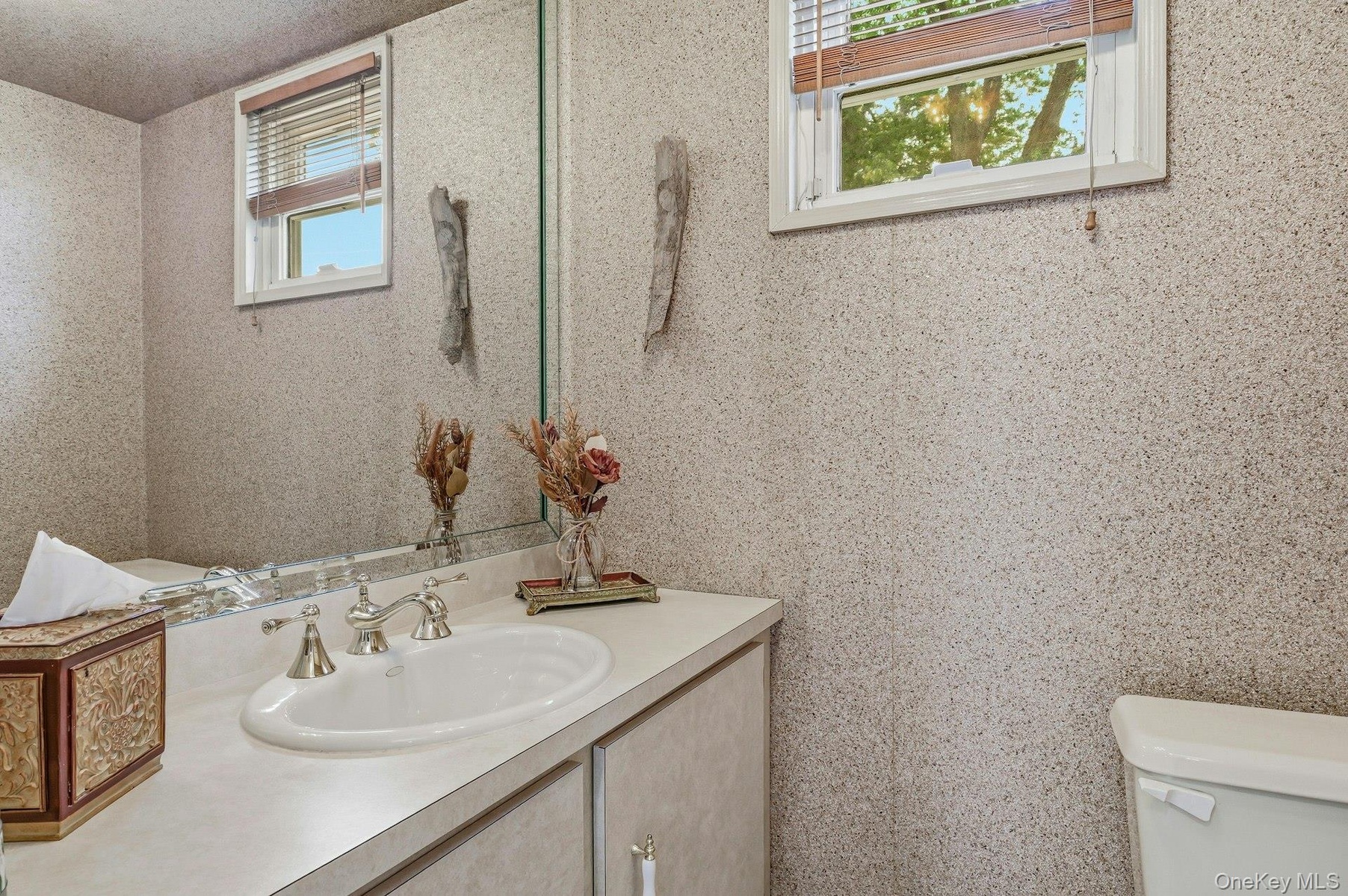 Bathroom vanity featuring an integrated sink with a chrome faucet, a large wall-mounted mirror, and a window with wood-finish blinds