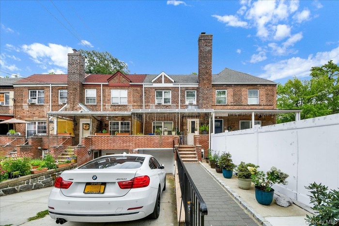 Brick exterior townhouse featuring a covered front entry, an attached garage, a paved driveway, a side walkway, and a privacy fence