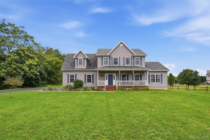 Two-story residence featuring a covered front porch, dormer windows, blue shutters, a dark blue front door, and a spacious front lawn