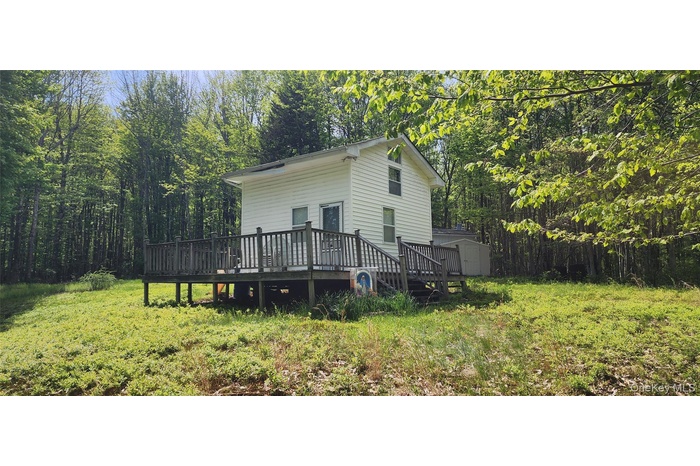 View of home's exterior with a storage unit, a wooden deck, an outdoor structure, and a view of trees