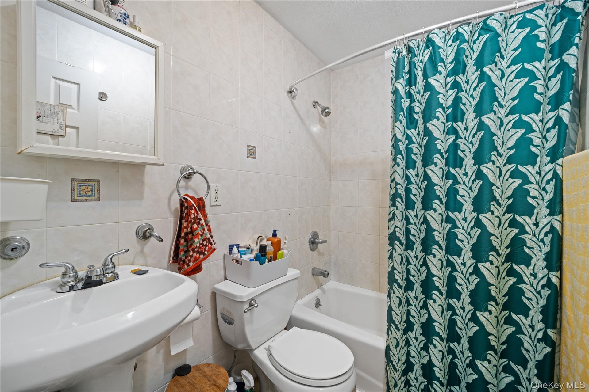 Bathroom featuring pedestal sink, chrome faucet, wall-mounted mirror, white ceramic tile, and a shower/tub combination