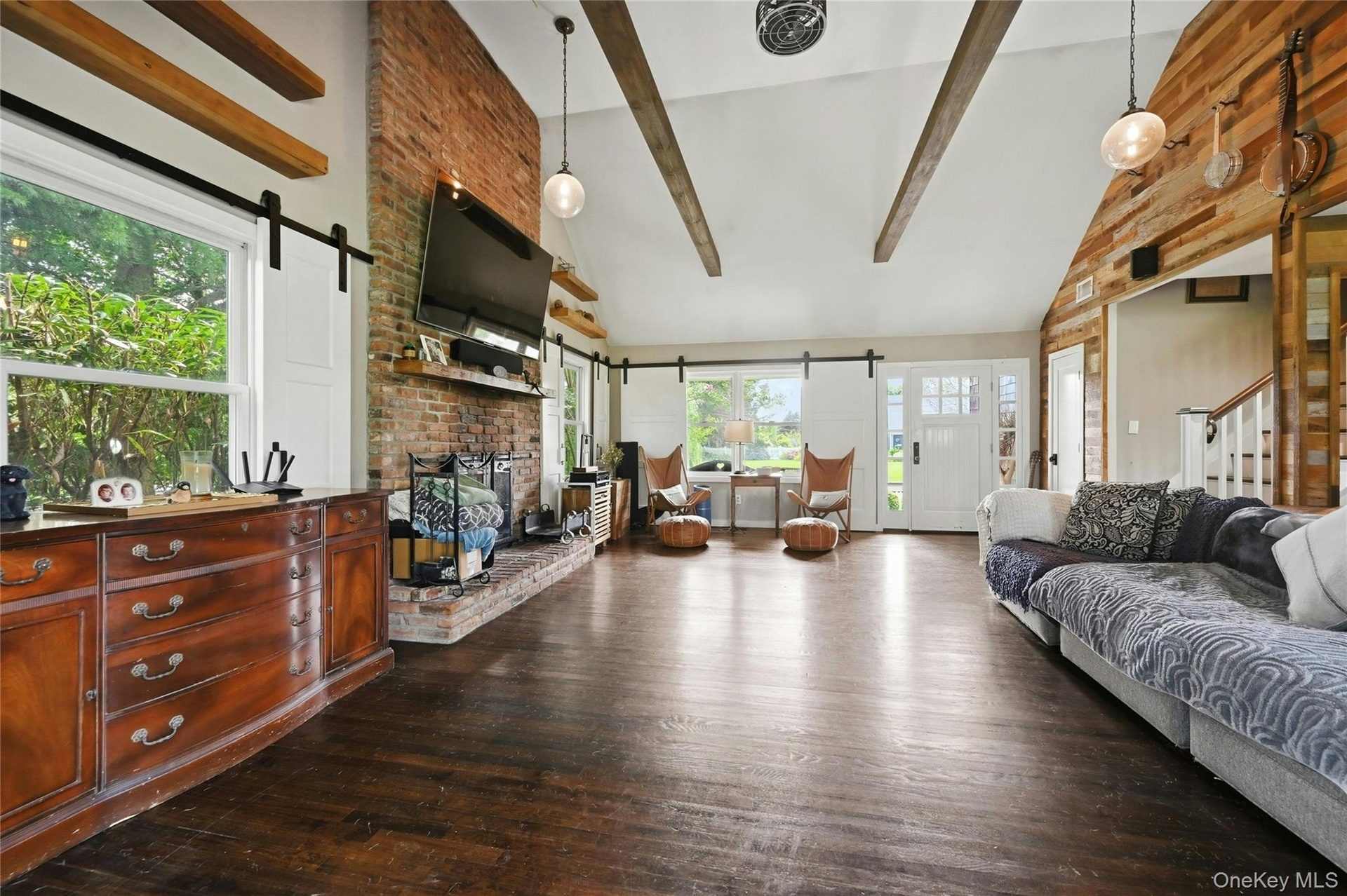 Spacious living area featuring exposed ceiling beams, a brick fireplace, wood-finish flooring, and a front entry door with side windows