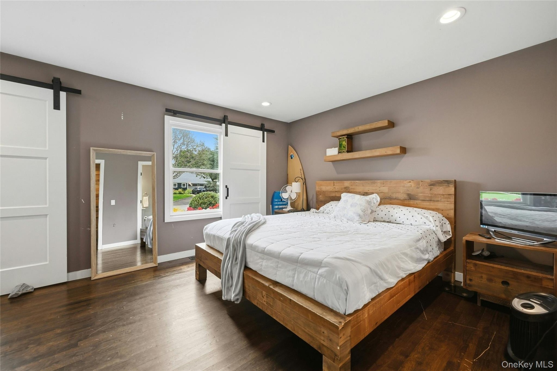 Spacious primary bed-room featuring dark wood-finish flooring, recessed lighting, and a window with white trim, plantation style shutter as window-tre