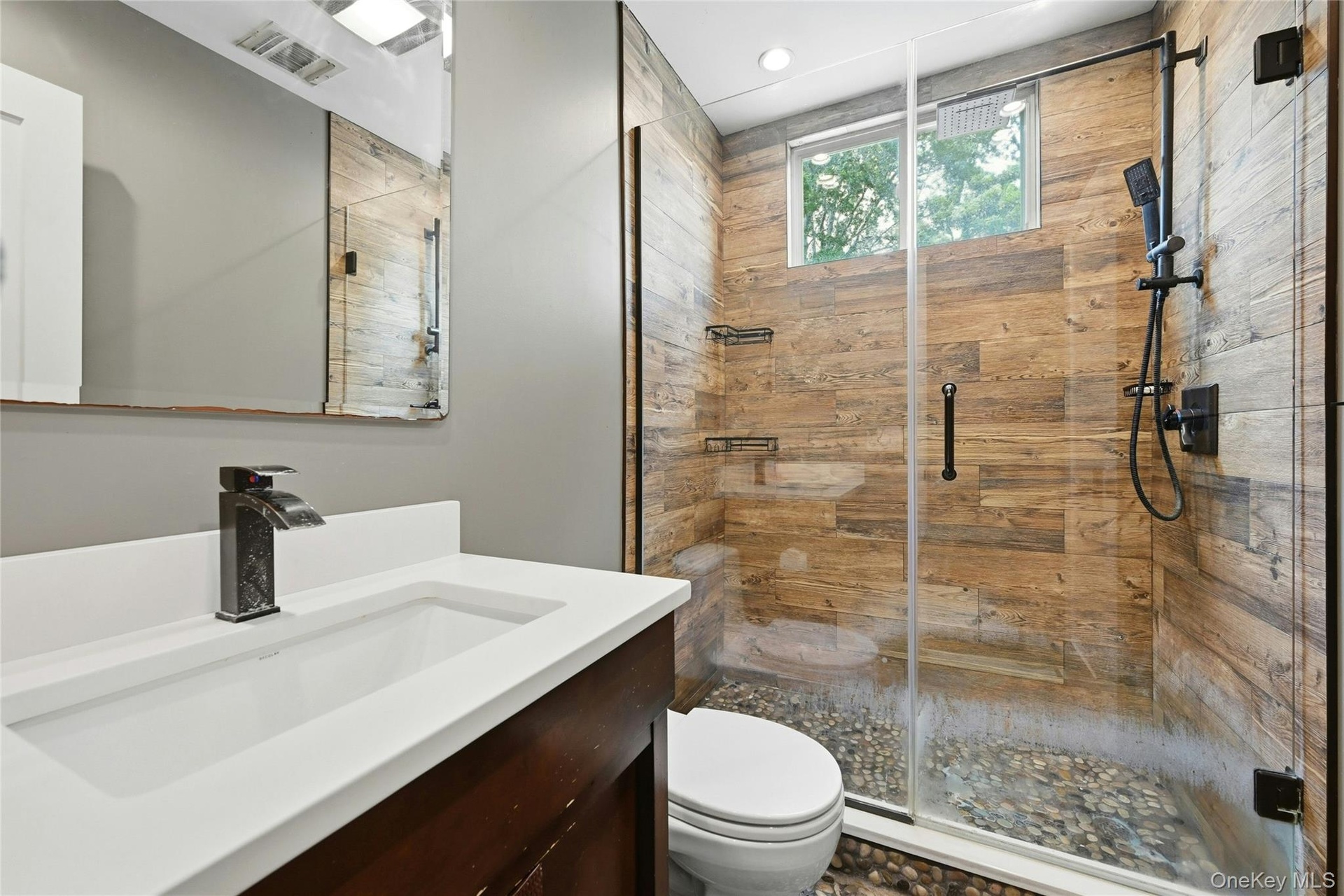 Walk-in shower featuring wood-finish wall tile, pebble floor, and glass enclosure