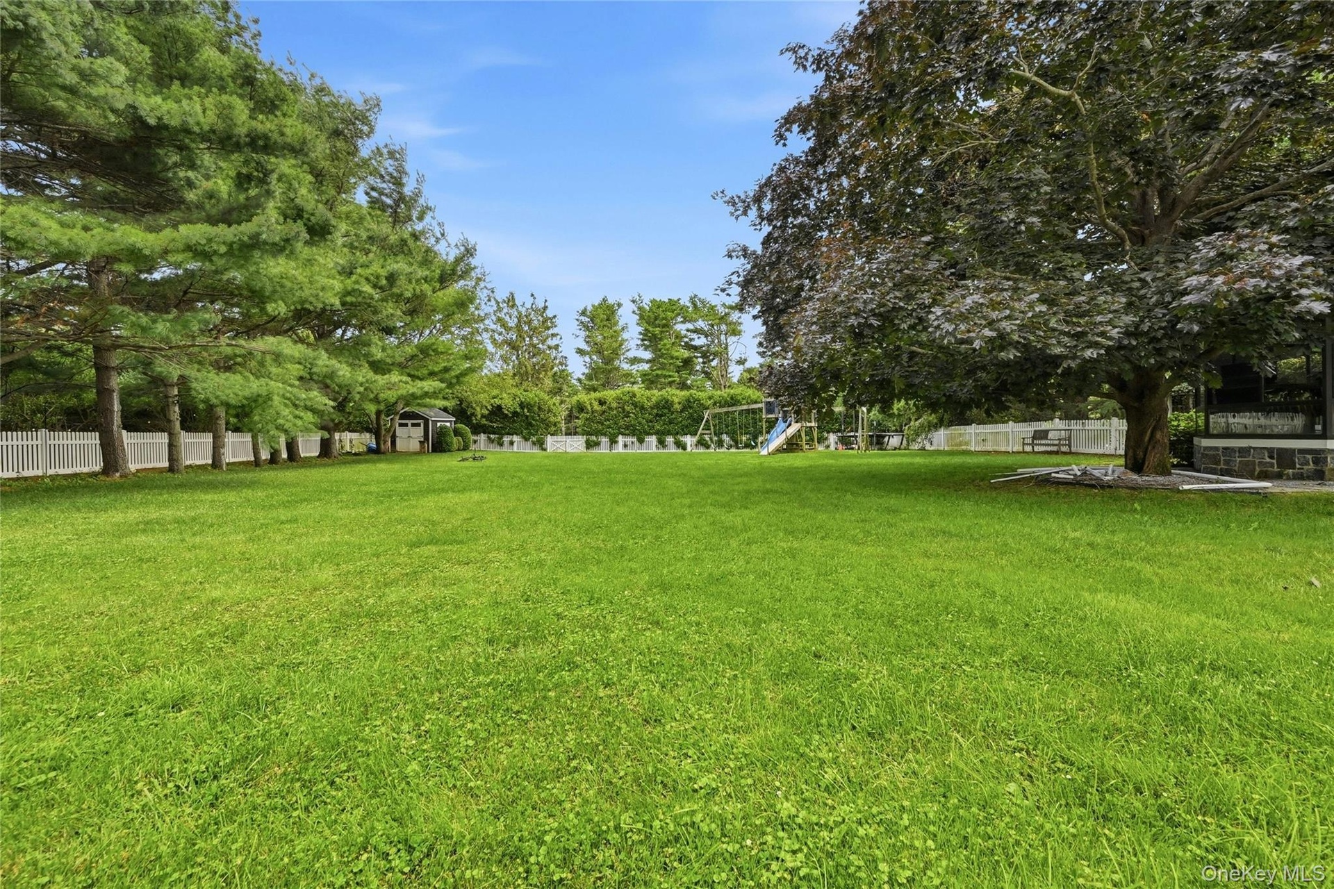 Expansive green lawn framed by mature trees and a white picket fence
