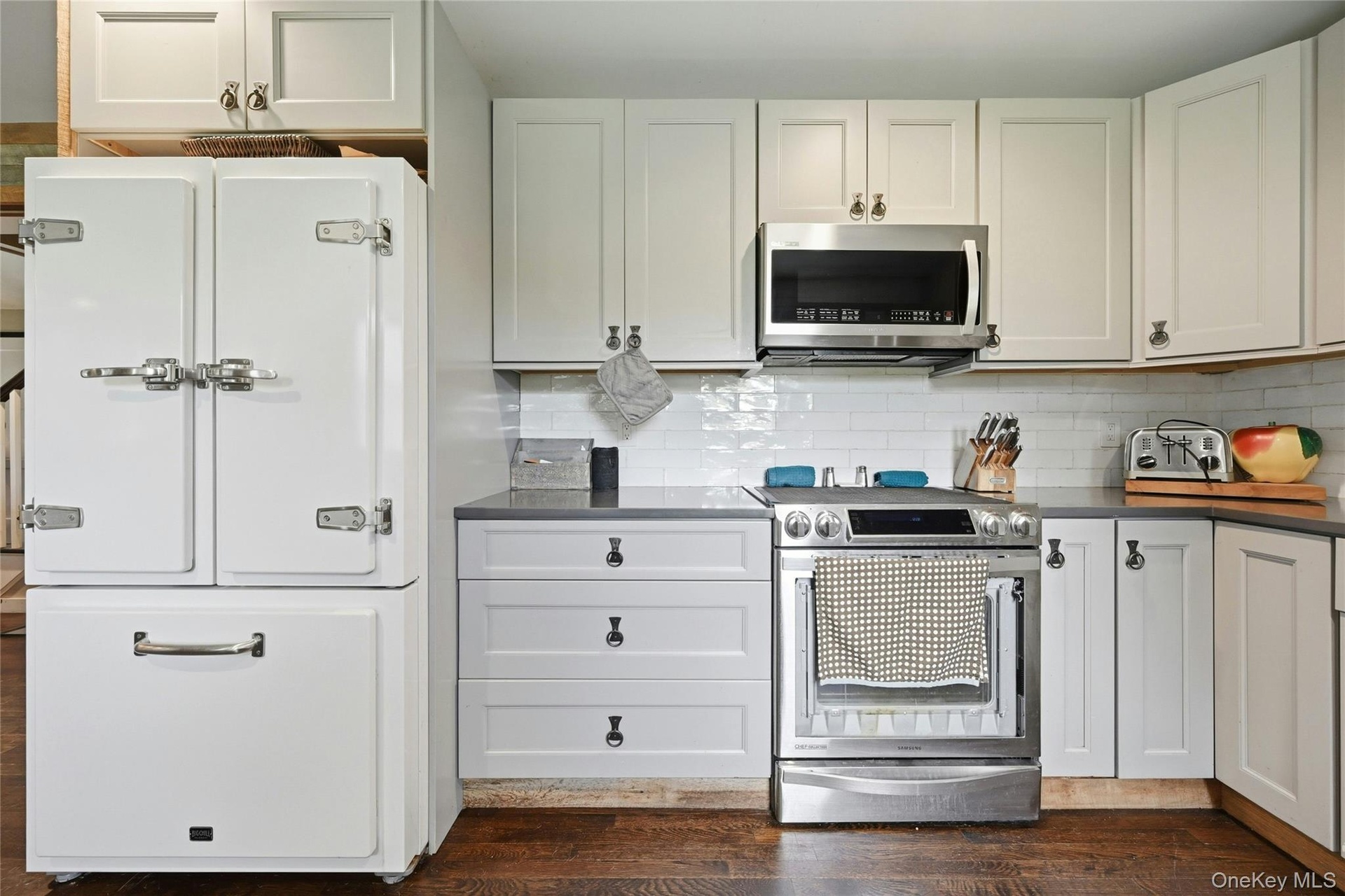 Kitchen featuring stainless steel appliances, white shaker-style cabinetry, dark countertops, a white subway tile backsplash, and wood-finish flooring