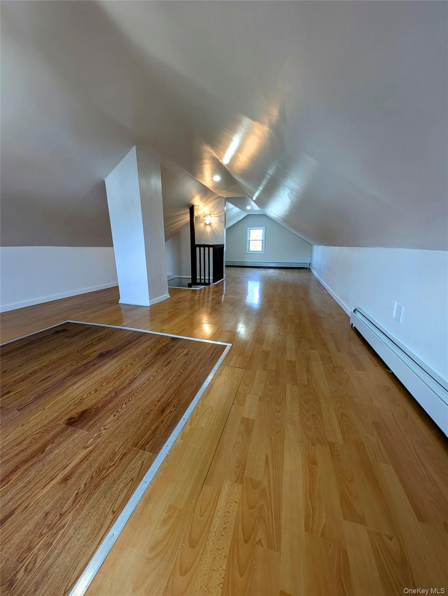 Additional living space featuring baseboards, a baseboard heating unit, vaulted ceiling, and wood finished floors