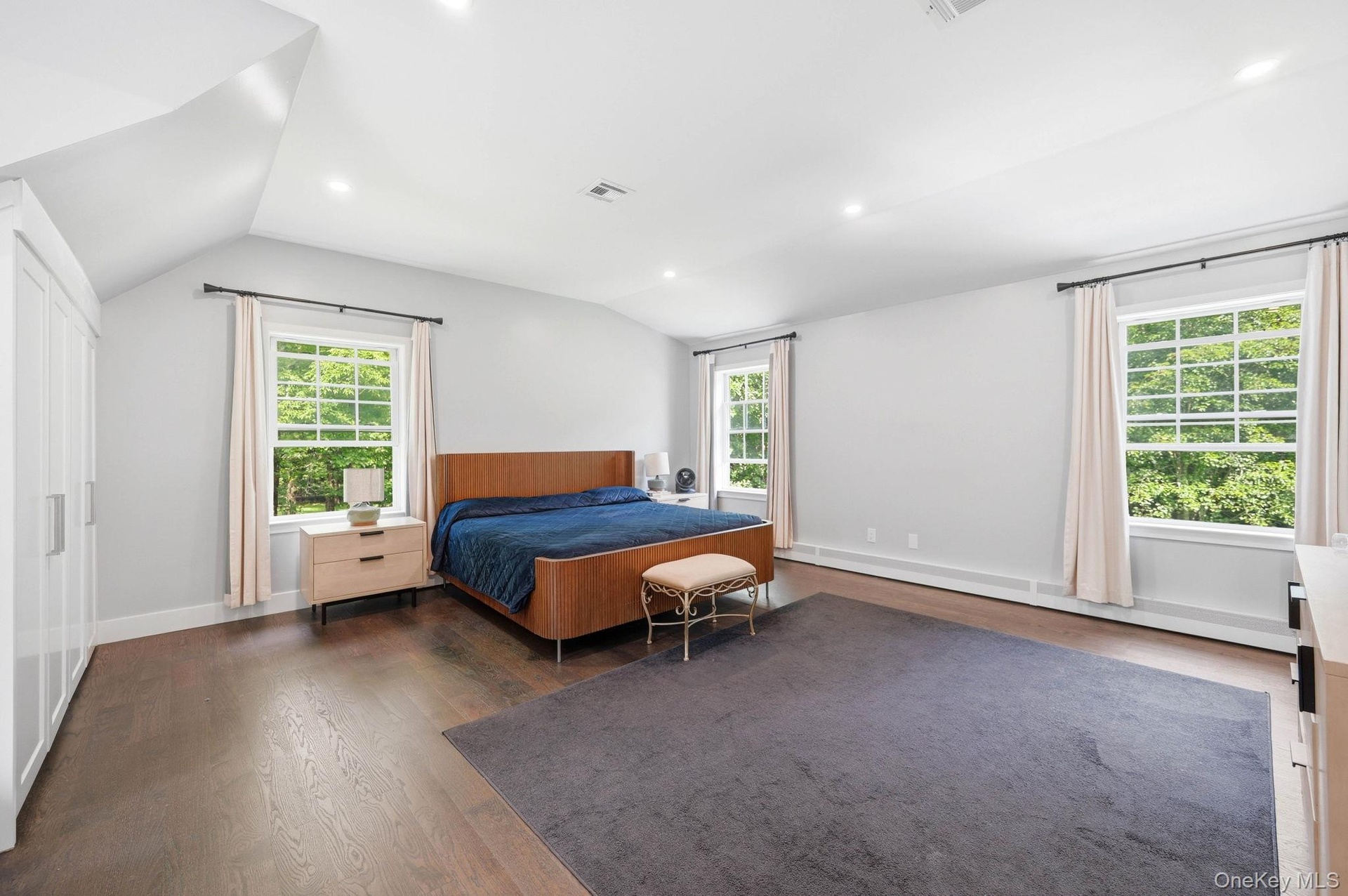 Spacious room featuring rich wood-finish flooring, white walls, and a vaulted ceiling with recessed lighting
