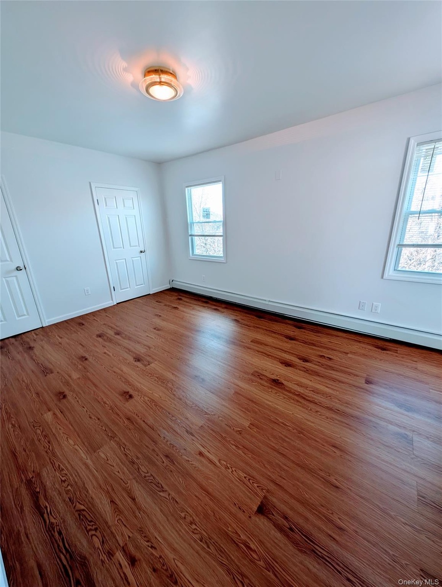 Unfurnished bedroom featuring a baseboard radiator, wood finished floors, and baseboards