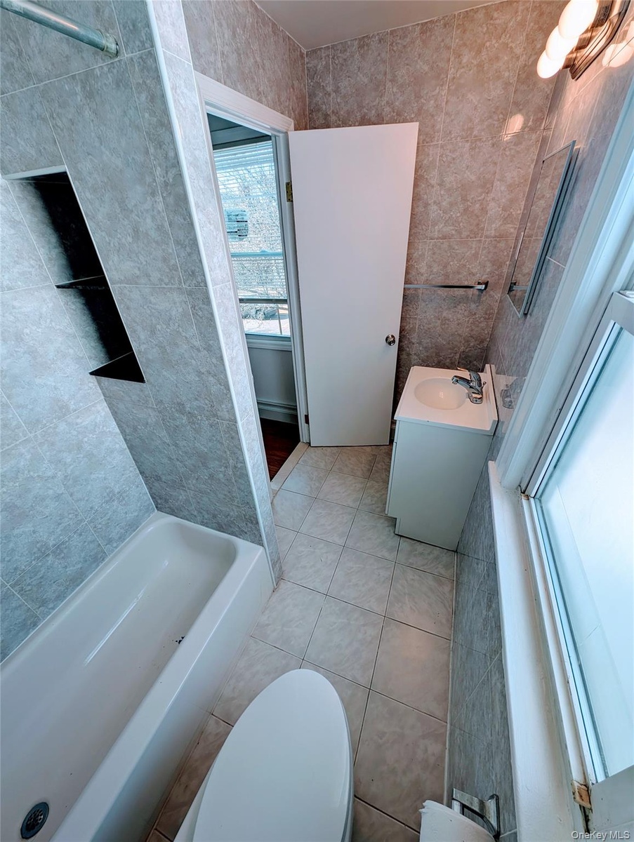 Bathroom featuring vanity, tile patterned floors, toilet, a tub to relax in, and tile walls