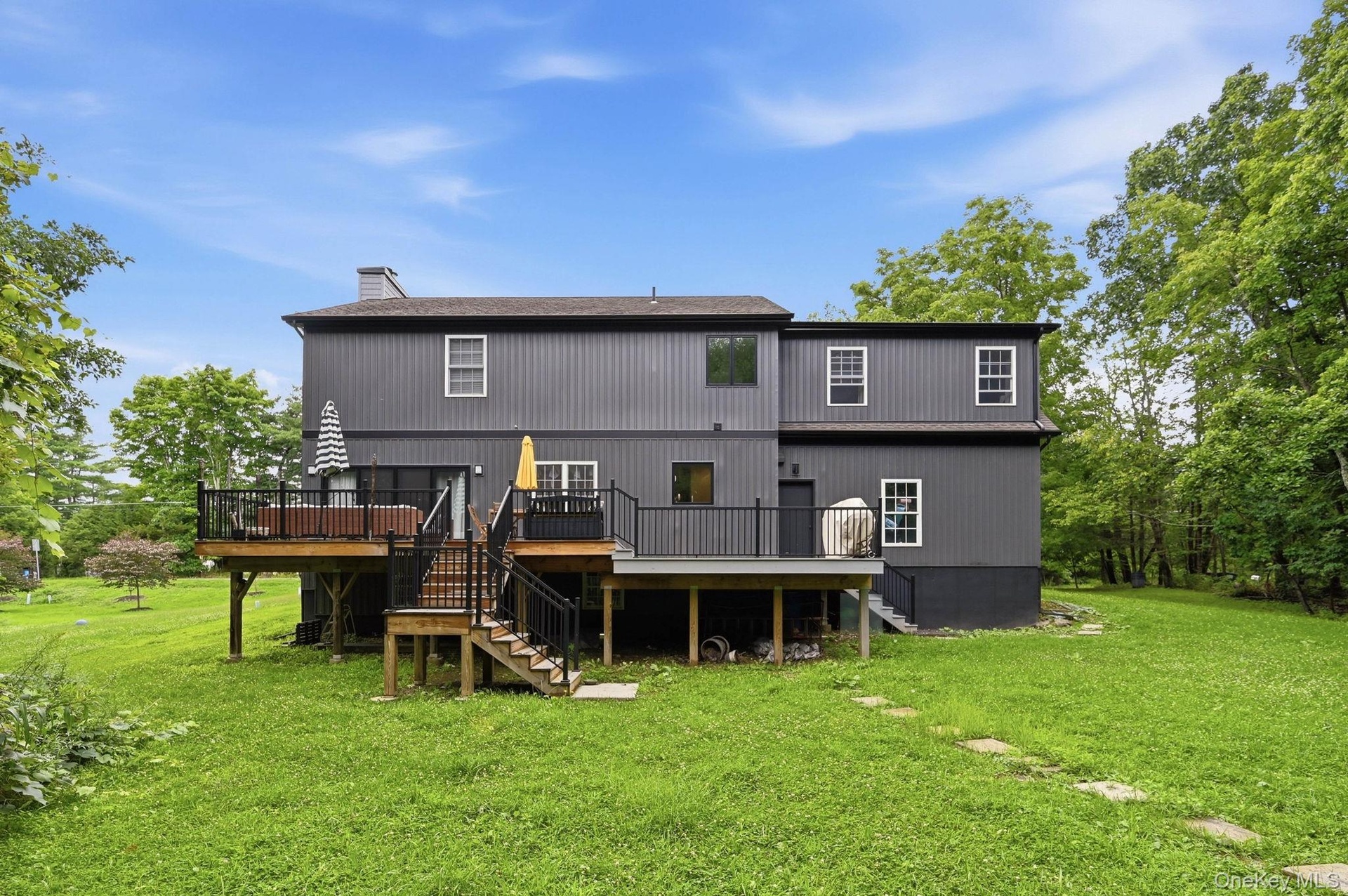 Rear exterior featuring a multi-level wood deck with black railings, a walk-out lower level, and a expansive grassy yard