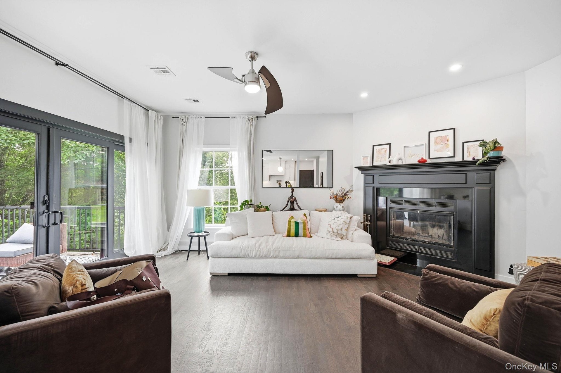 A bright and inviting family room featuring rich hardwood floors, recessed lighting and a contemporary ceiling fan. A striking fireplace with a bold d