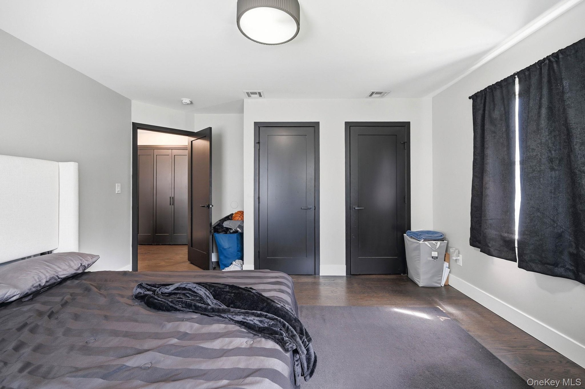 Spacious room featuring dark wood-finish flooring, light grey walls, and white baseboards