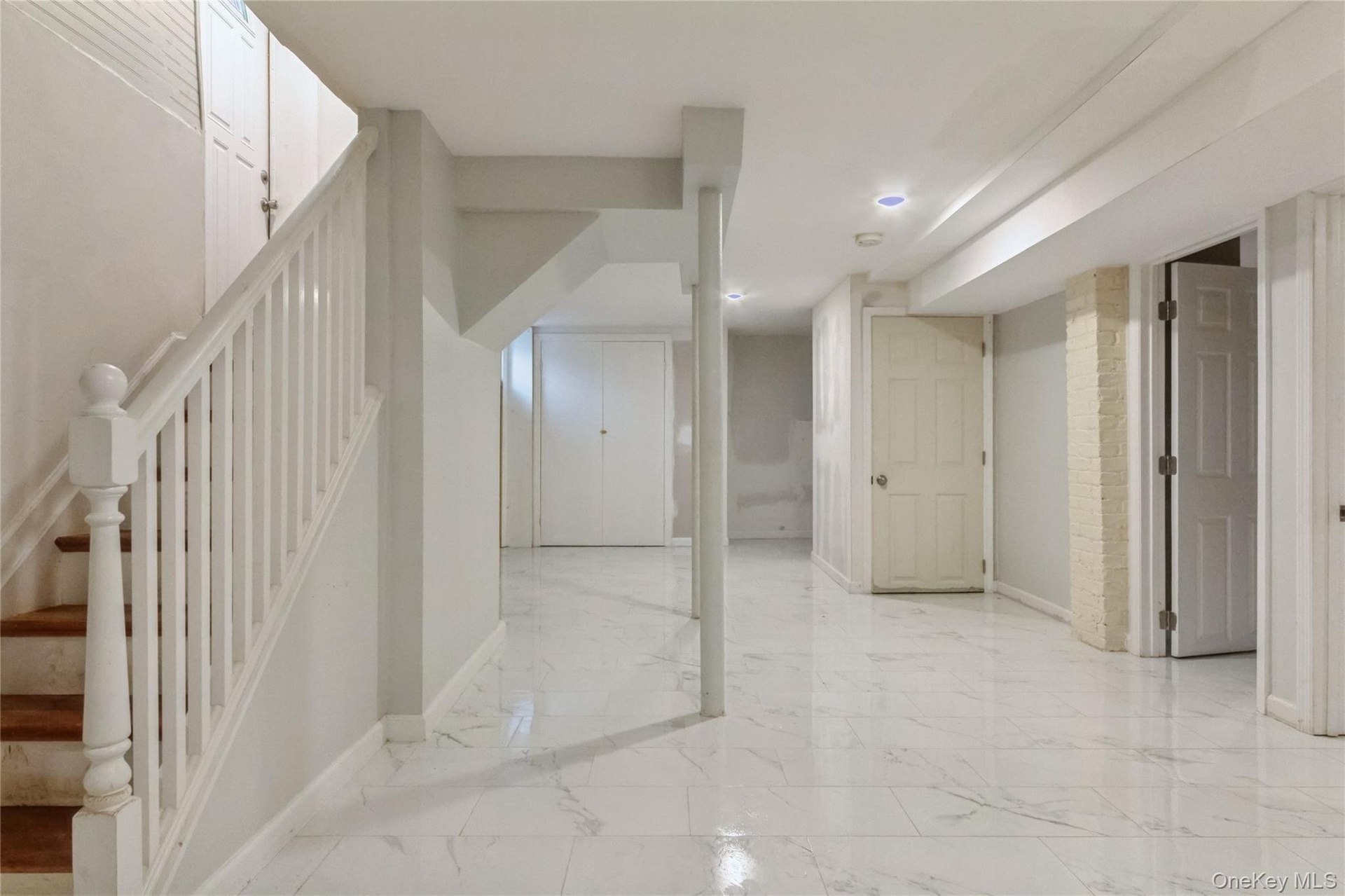 Finished basement space featuring white marble-look tile flooring, recessed ceiling lighting, a white painted staircase with wood treads, and multiple