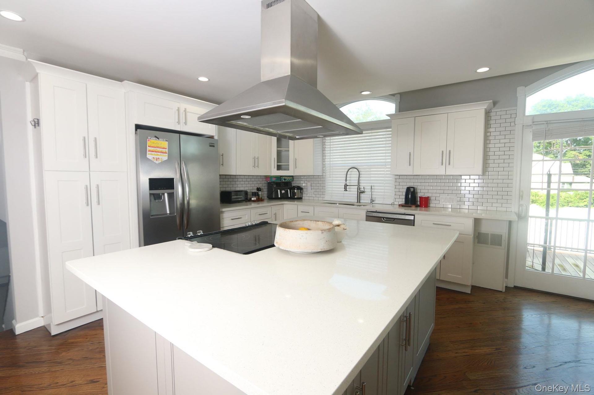 Spacious kitchen featuring an expansive center island, white cabinetry, a stainless steel refrigerator, a professional-grade range hood, and wood-fini