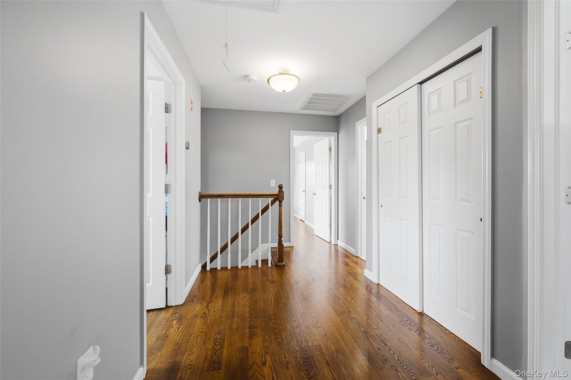 Hallway featuring wood-finish flooring, white paneled doors, and a wood railing with white spindles