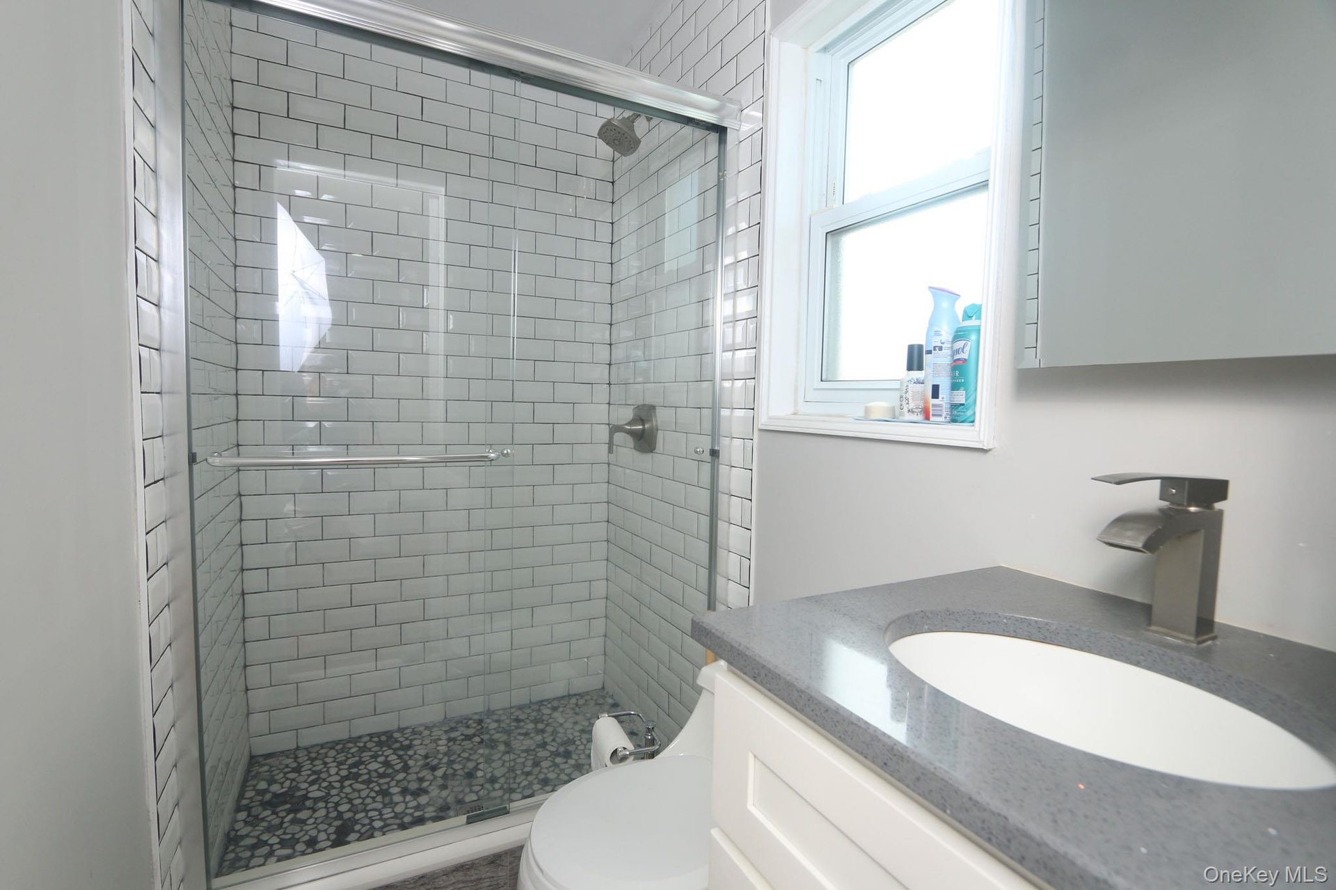 Bathroom featuring a subway tile shower with pebble flooring and clear glass enclosure