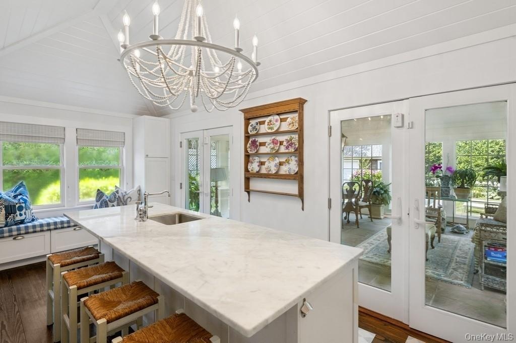 Kitchen with french doors, plenty of natural light, light stone countertops, a center island with sink, and vaulted ceiling