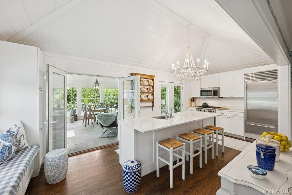 Kitchen featuring stainless steel appliances, a chandelier, dark wood-style floors, white cabinetry, and an island with sink