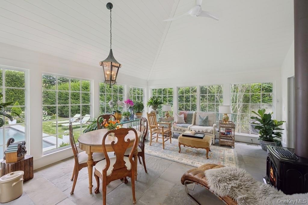 Sunroom / solarium featuring vaulted ceiling, plenty of natural light, a wood stove, and stone tile flooring