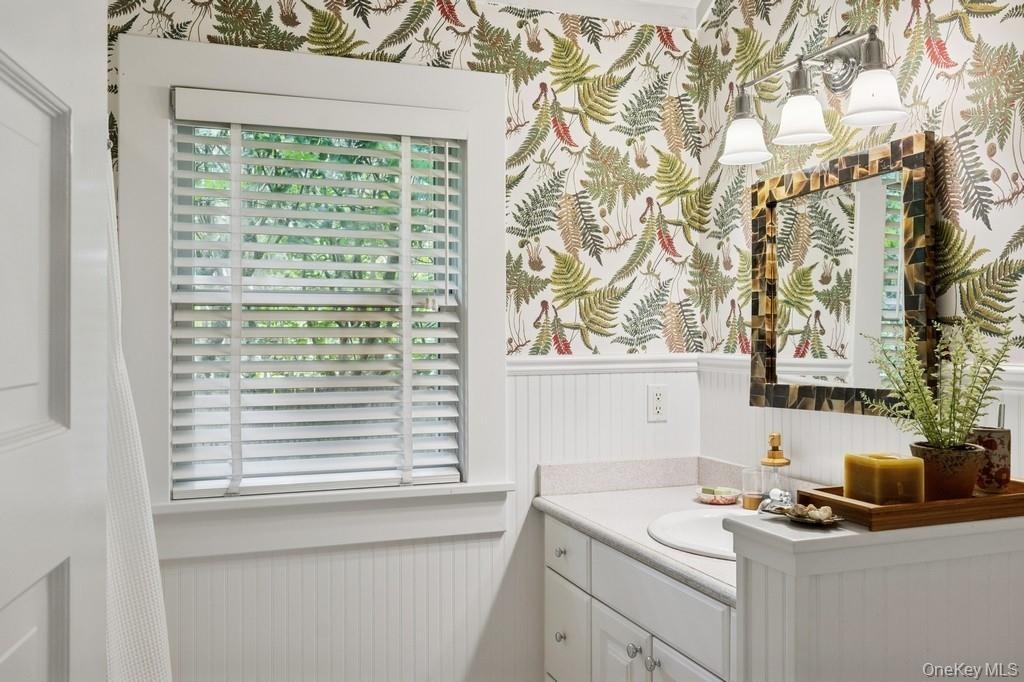 Bathroom with wainscoting, vanity, and wallpapered walls