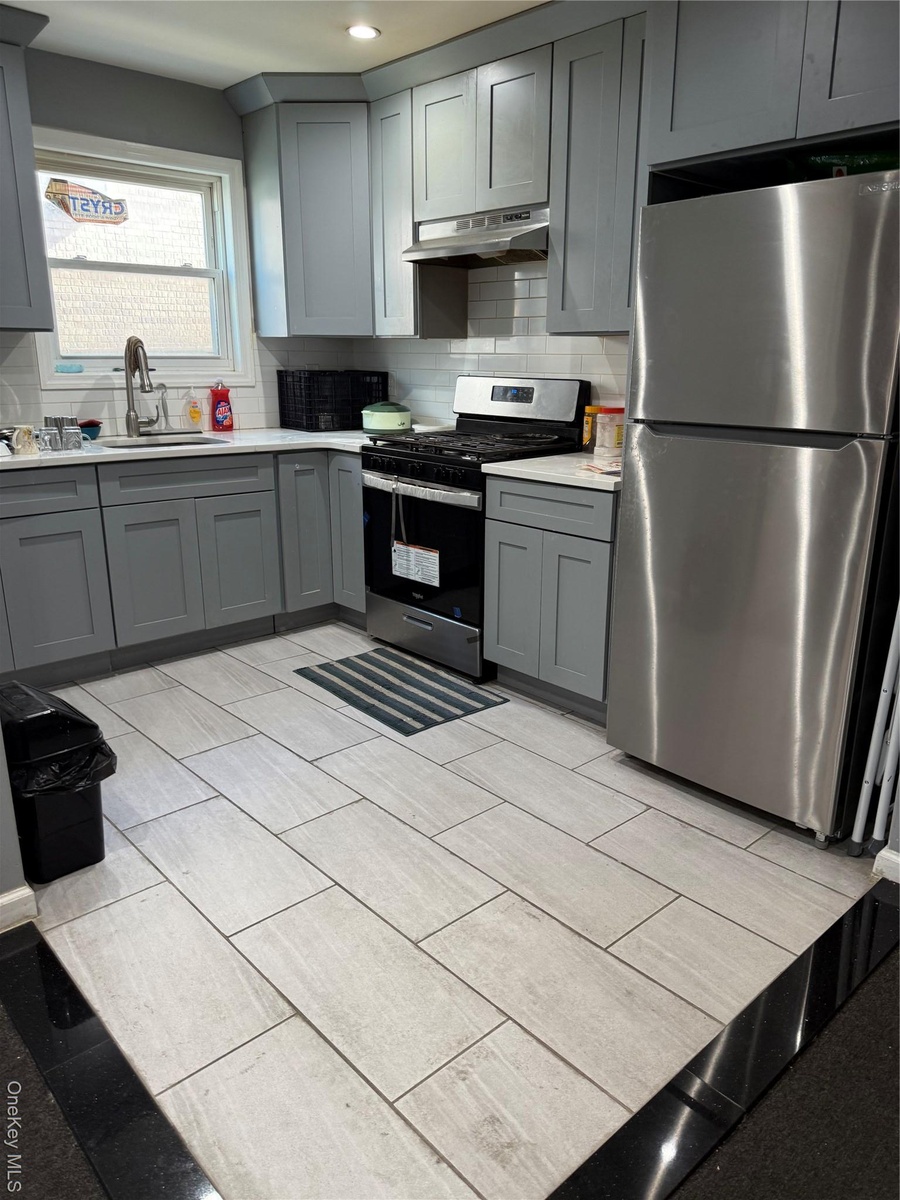 Kitchen with gray cabinets, fridge, stainless steel stove, decorative backsplash, and recessed lighting