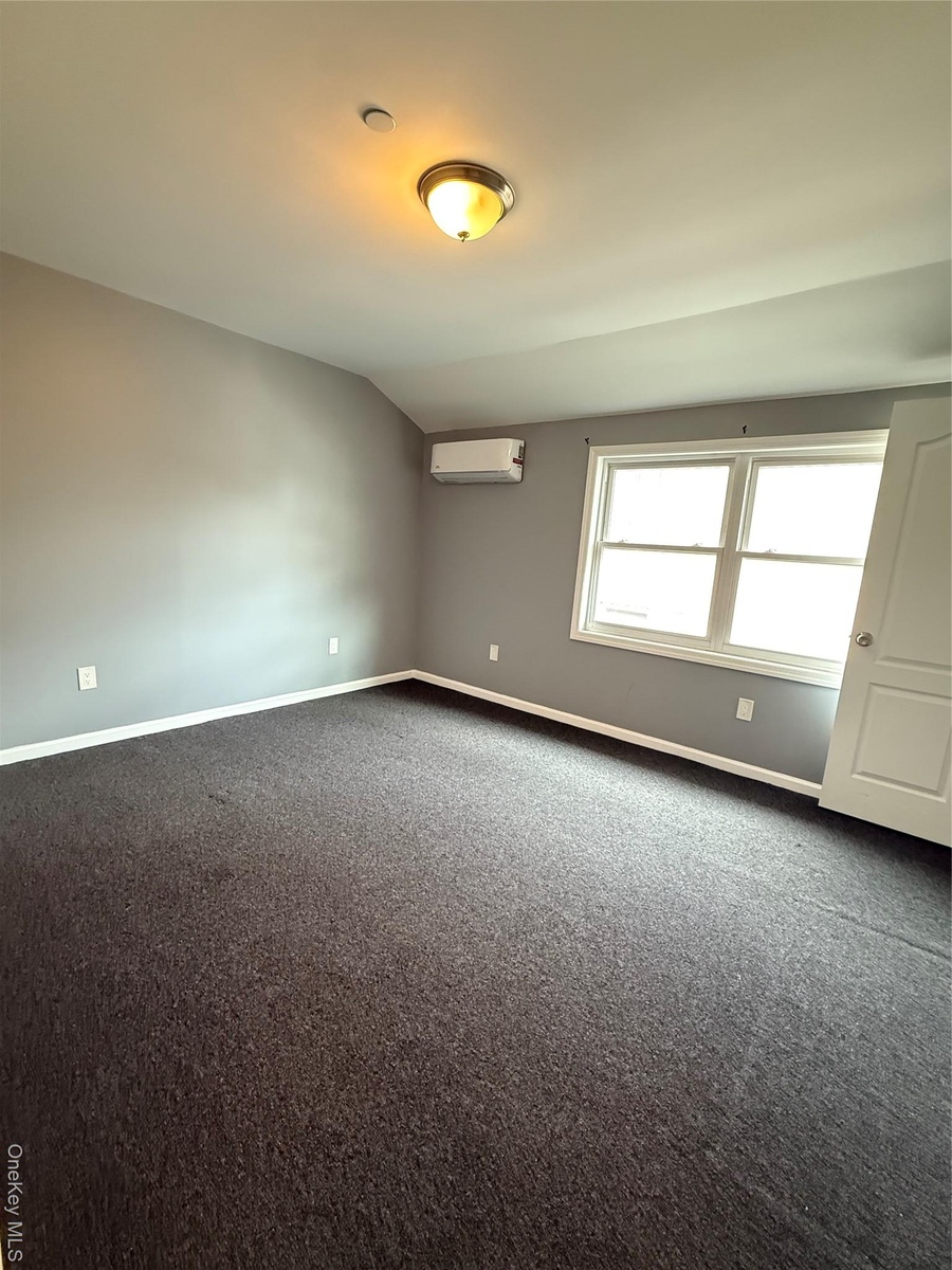 Spare room featuring dark colored carpet and lofted ceiling