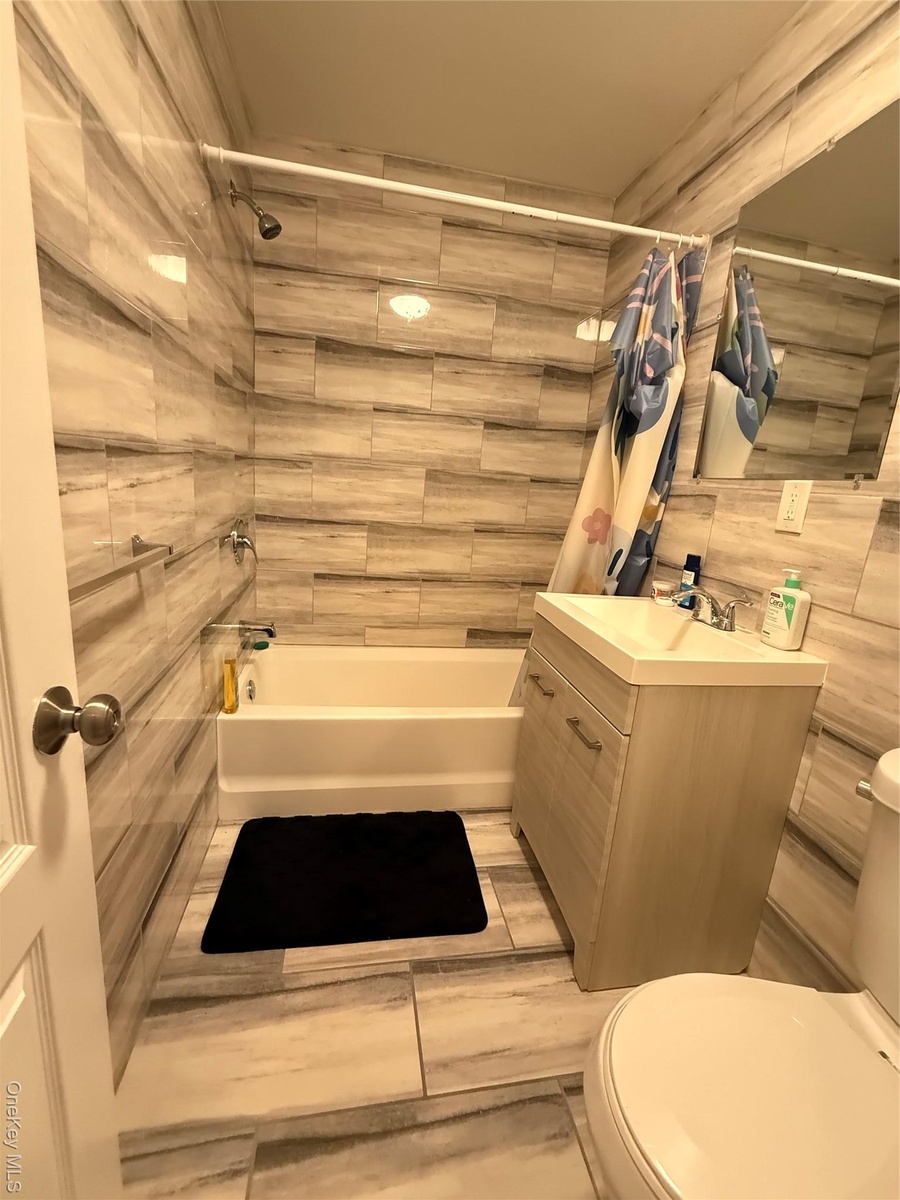Bathroom featuring vanity, shower / bath combo with shower curtain, and tile walls