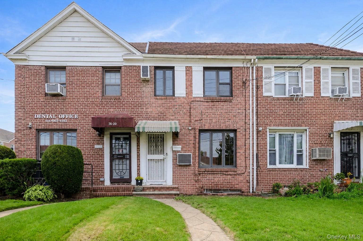 Brick facade with multiple window styles, two awnings, and a concrete pathway