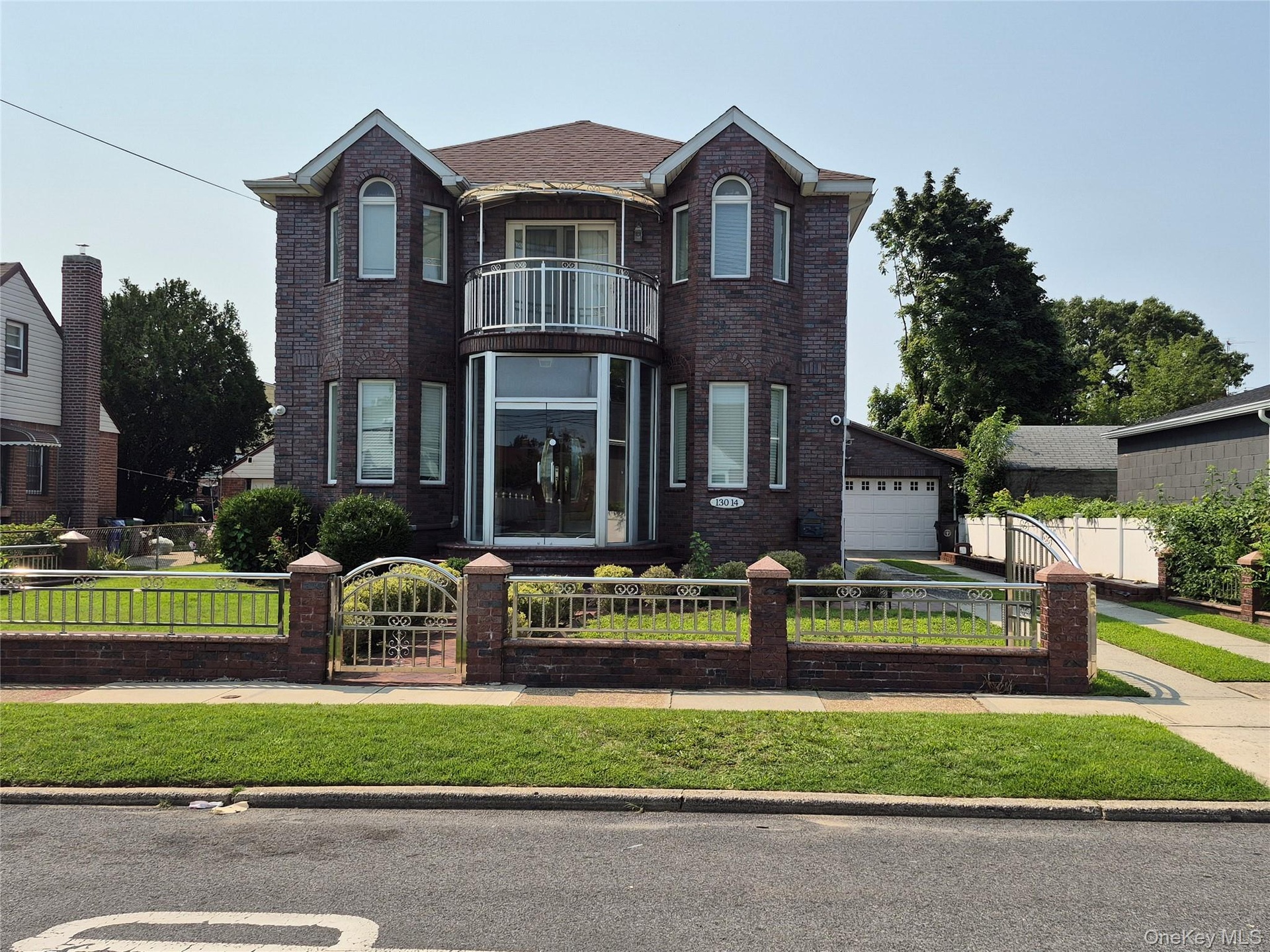 Brick exterior featuring a Juliet balcony with metal railing, arched windows, and full glass entryway with double doors.  Fenced in yard with brick an