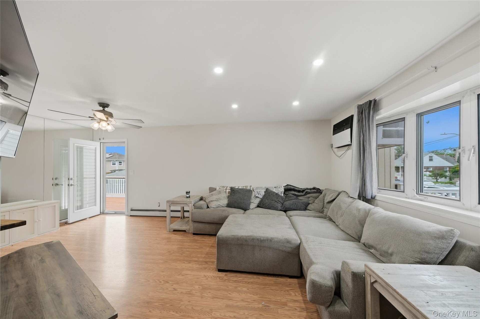 Bright open-concept living area featuring a sectional sofa arrangement, wood-finish flooring throughout, and abundant natural light from large multi-p