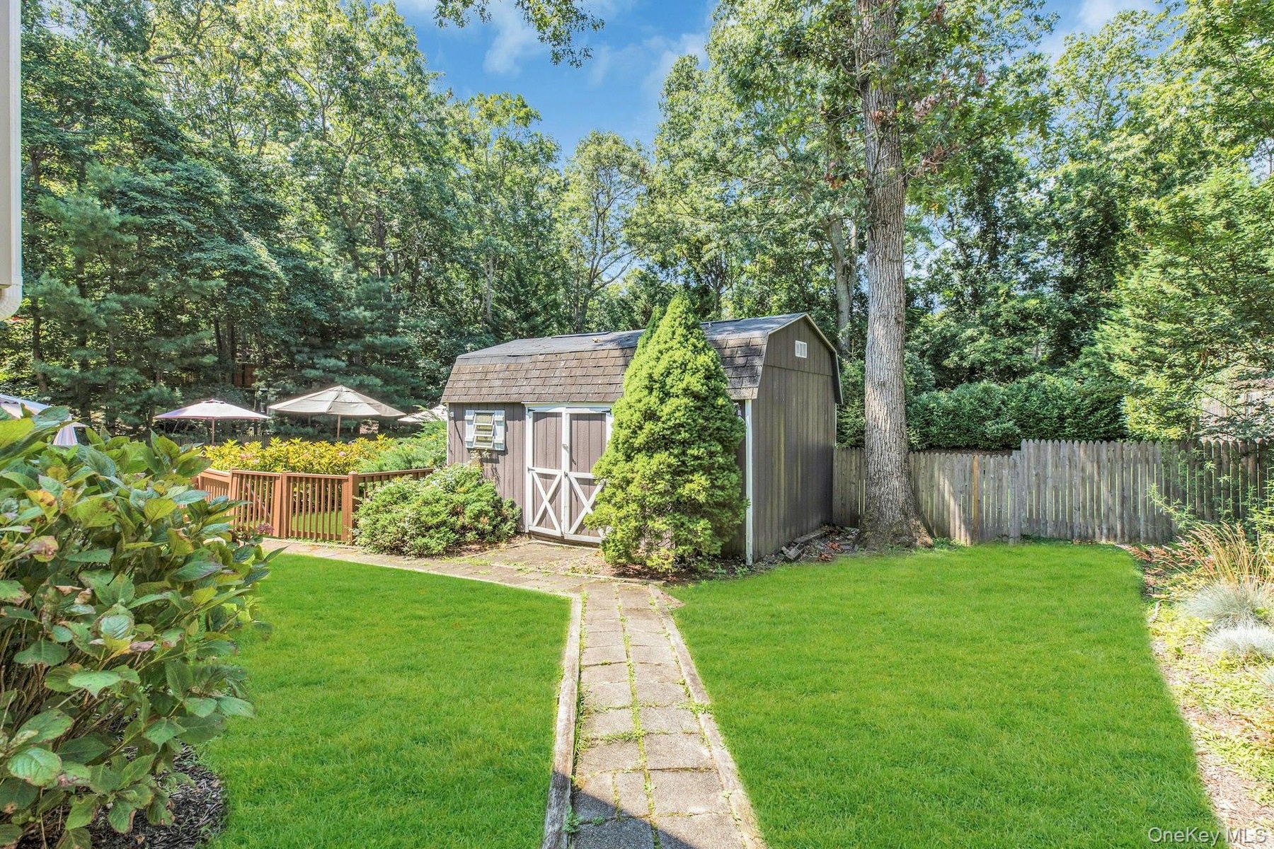 Expansive backyard oasis featuring a meticulously manicured lawn, mature tree-lined perimeter, and charming detached storage shed with X-brace detaili