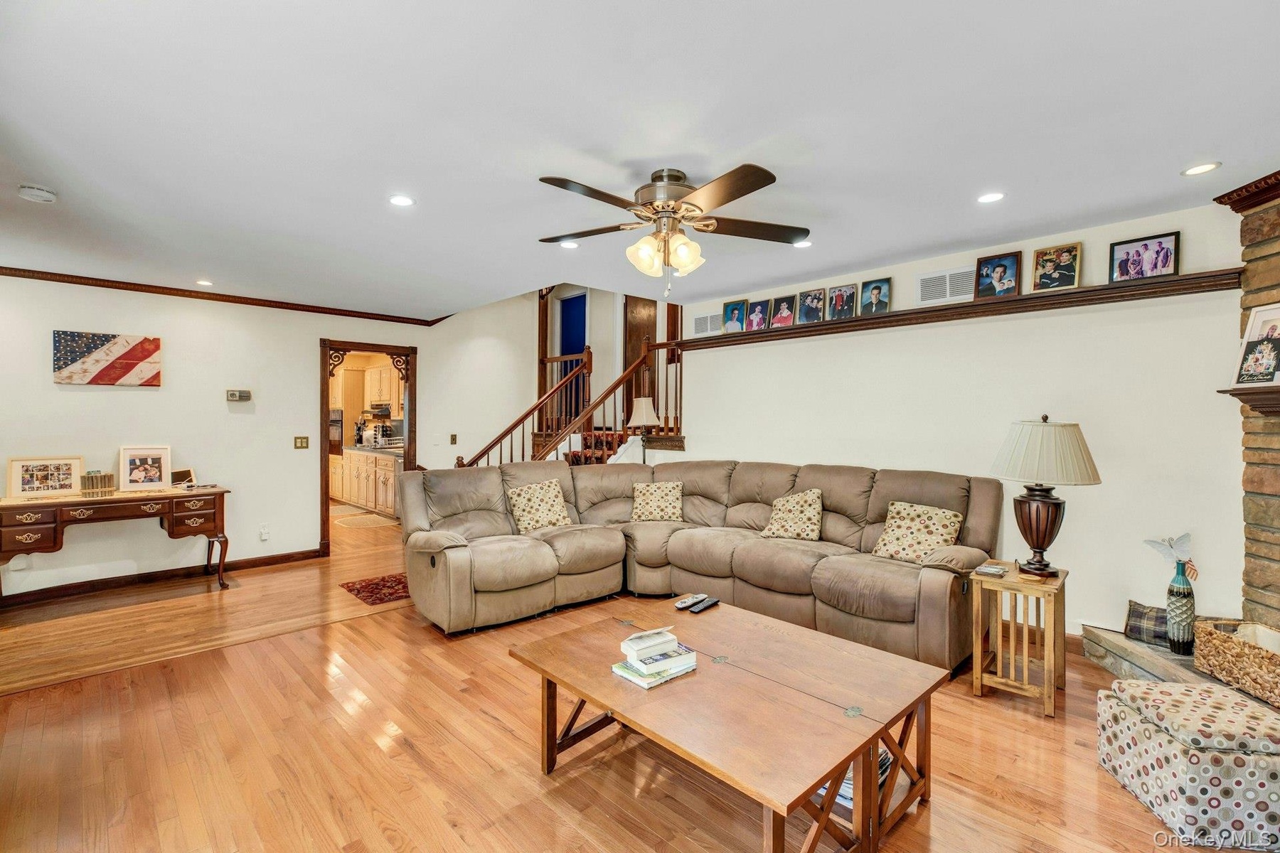 Spacious open-concept living area showcasing hardwood flooring, a neutral upholstered sectional sofa, coffered ceiling with ceiling fan, recessed ligh
