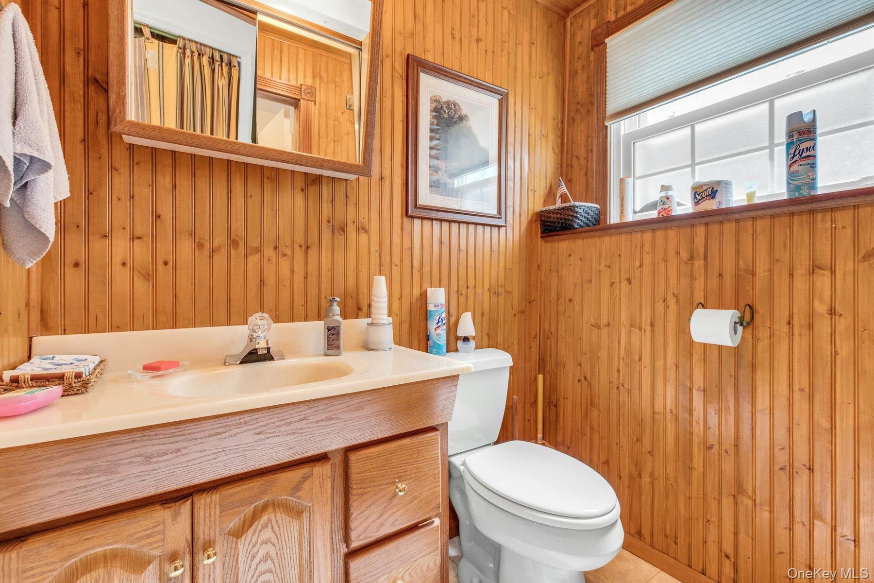 Warm wood-paneled bathroom featuring a wood-finish vanity with integrated sink, ceramic countertop, and ample storage cabinetry