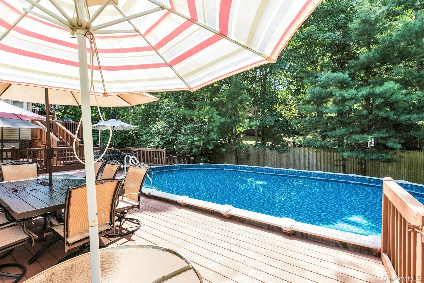 Expansive outdoor deck featuring an above-ground pool, wood fencing, and mature trees