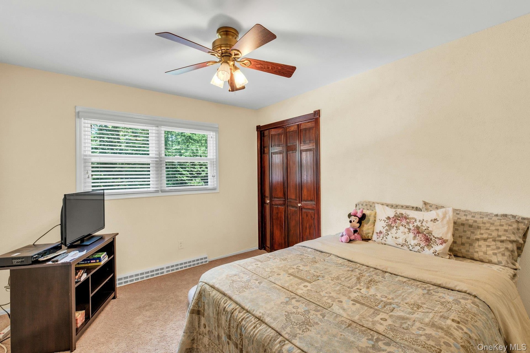 Bedroom featuring a ceiling fan with integrated lighting, a window with blinds, baseboard heating, and wood-paneled bifold closet doors