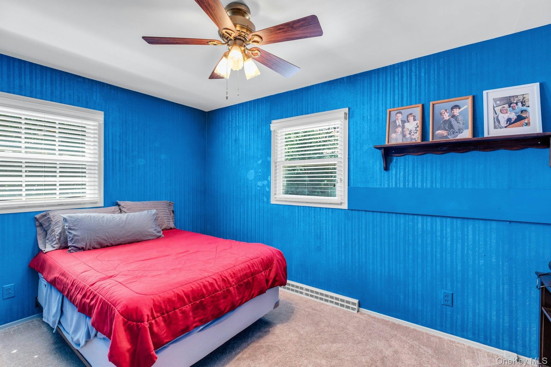Bright bedroom retreat showcasing vibrant blue textured wall paneling, carpeted flooring, and dual casement windows with plantation shutters