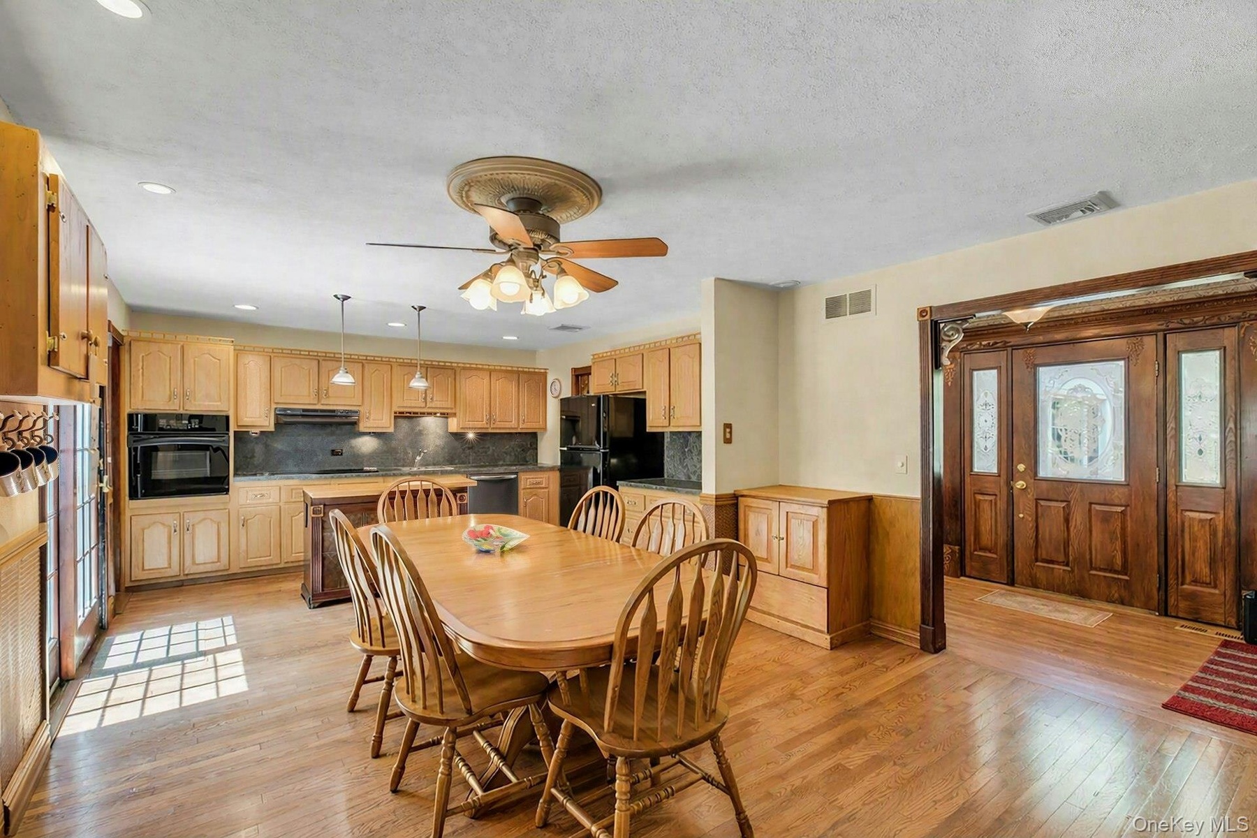 Spacious kitchen and dining area featuring warm wood cabinetry, stainless steel appliances, wood-finish flooring throughout, a ceiling fan with integr