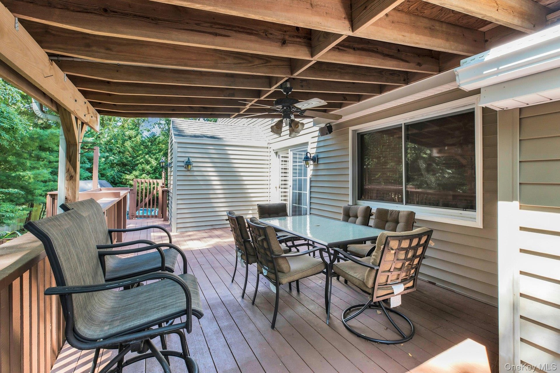 Expansive covered deck featuring wood-finish flooring, exposed wood beams, a ceiling fan, and direct access to interior spaces through a sliding glass