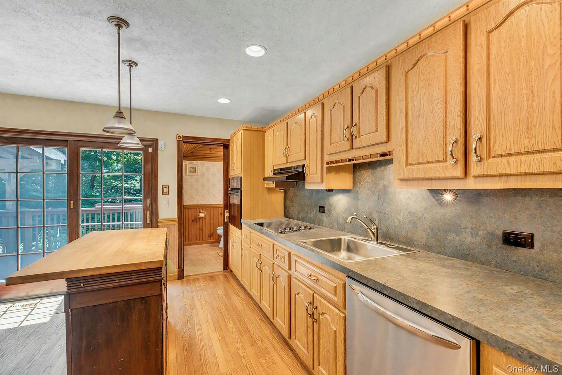 Kitchen featuring light wood cabinetry, a stainless steel dishwasher, a double basin sink, and pendant lighting