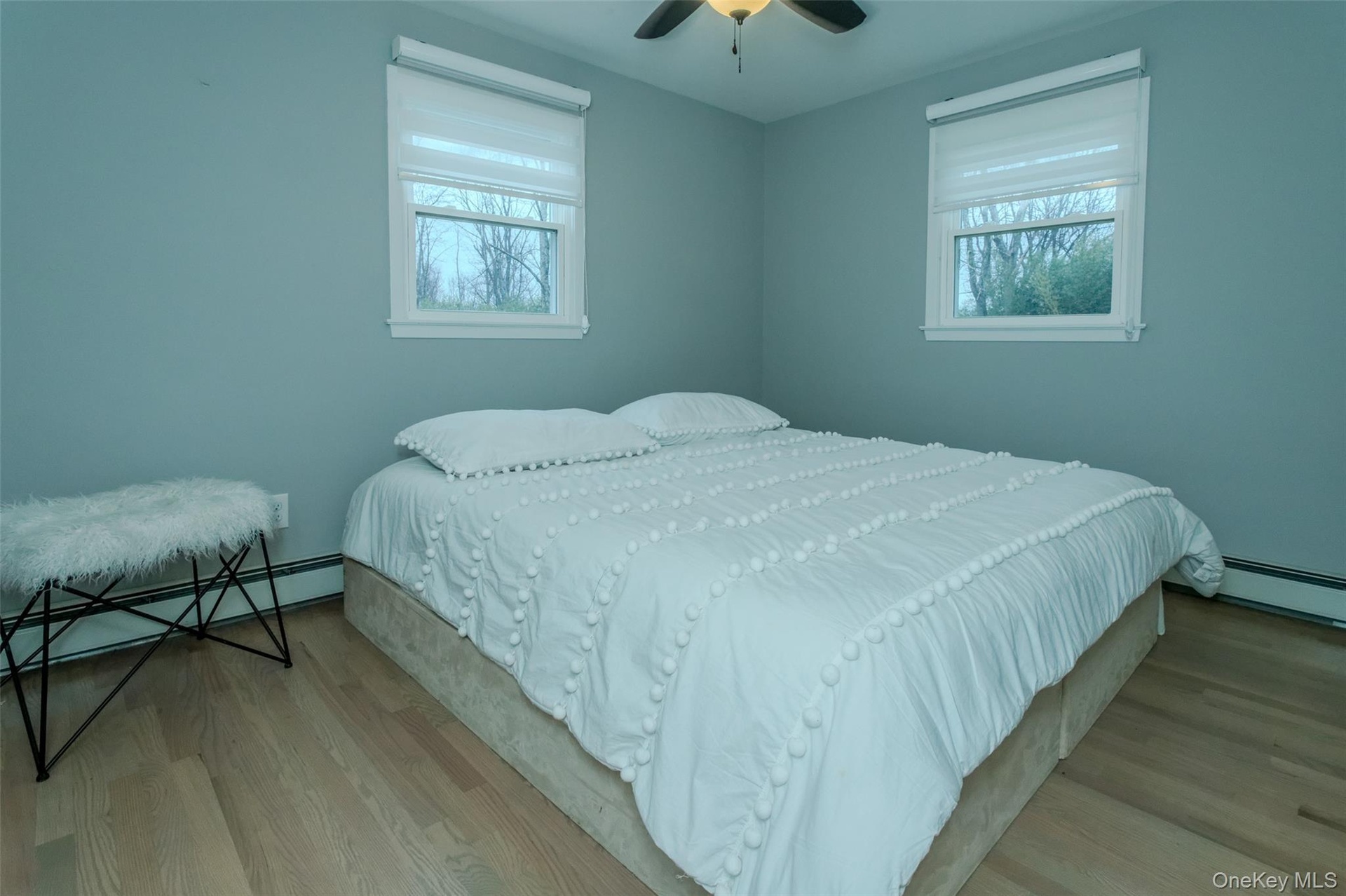 Bedroom with ceiling fan, light hardwood / wood-style floors, baseboard heating, and multiple windows