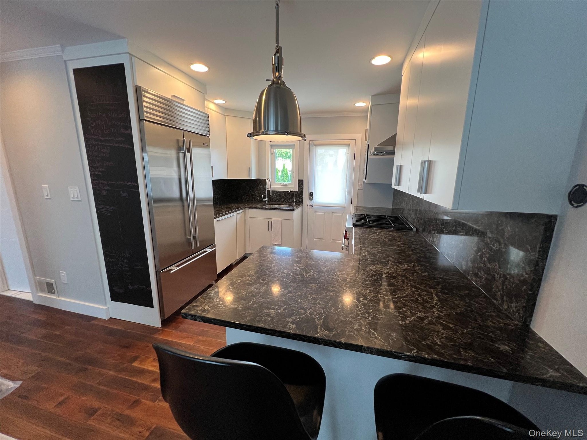 Sleek, modern kitchen featuring stainless steel appliances, white cabinetry, and a spacious granite-look countertop island with seating for two